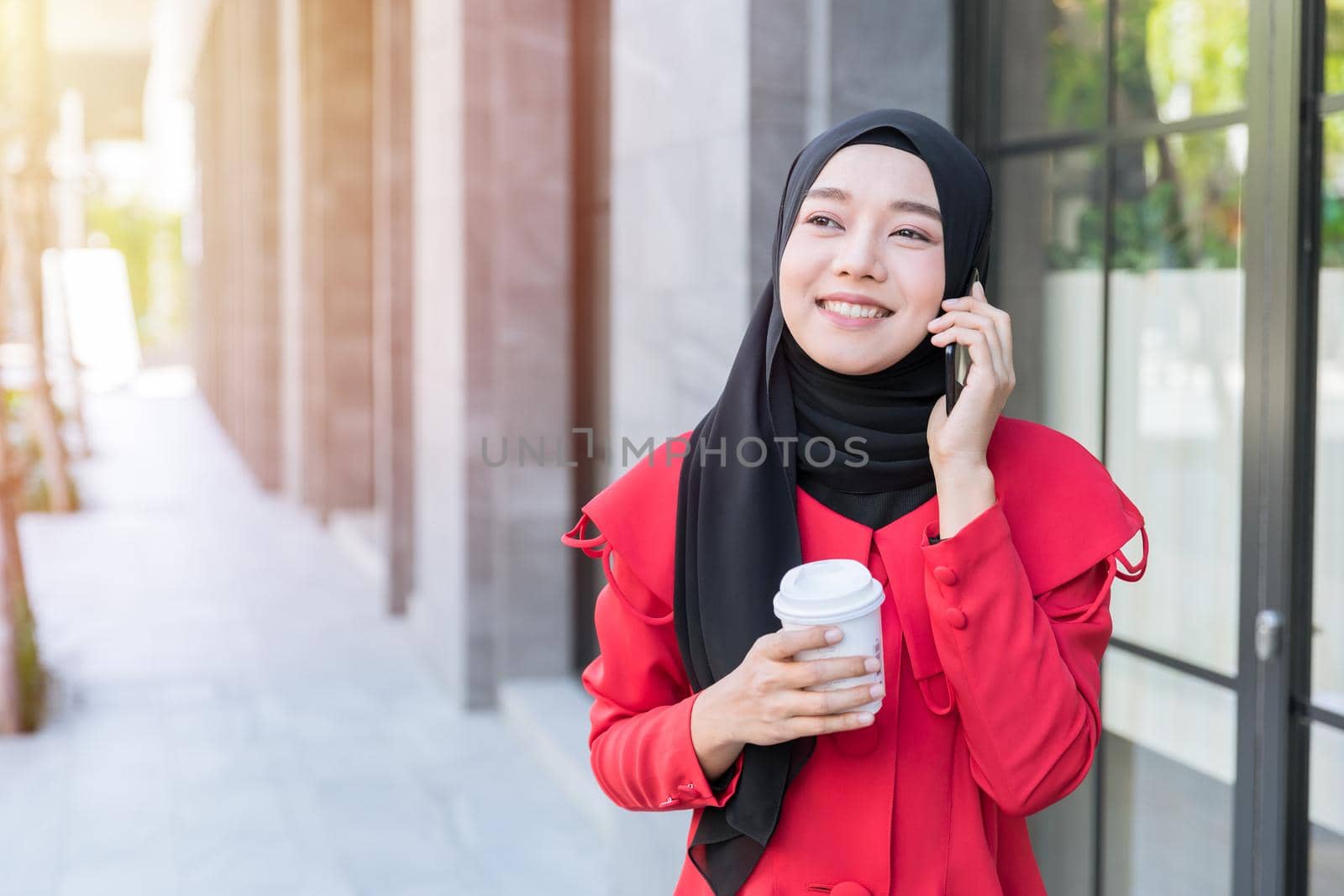 Asian Muslim Business woman happy using smartphone phone call contact customer while walking at the street with coffee cup by qualitystocks