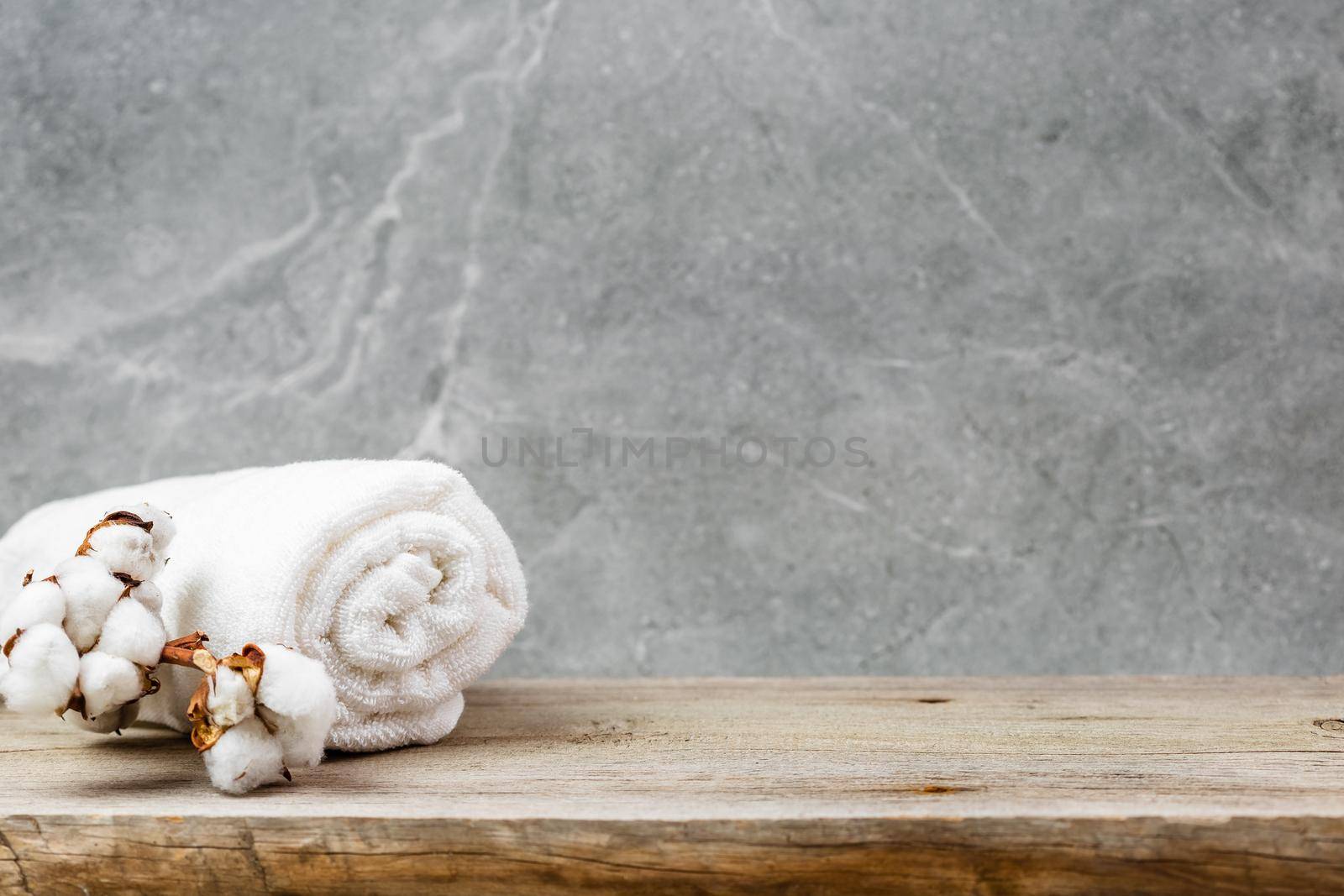 White cotton towel rolled up and cotton plant flower branch over grey marble wall background