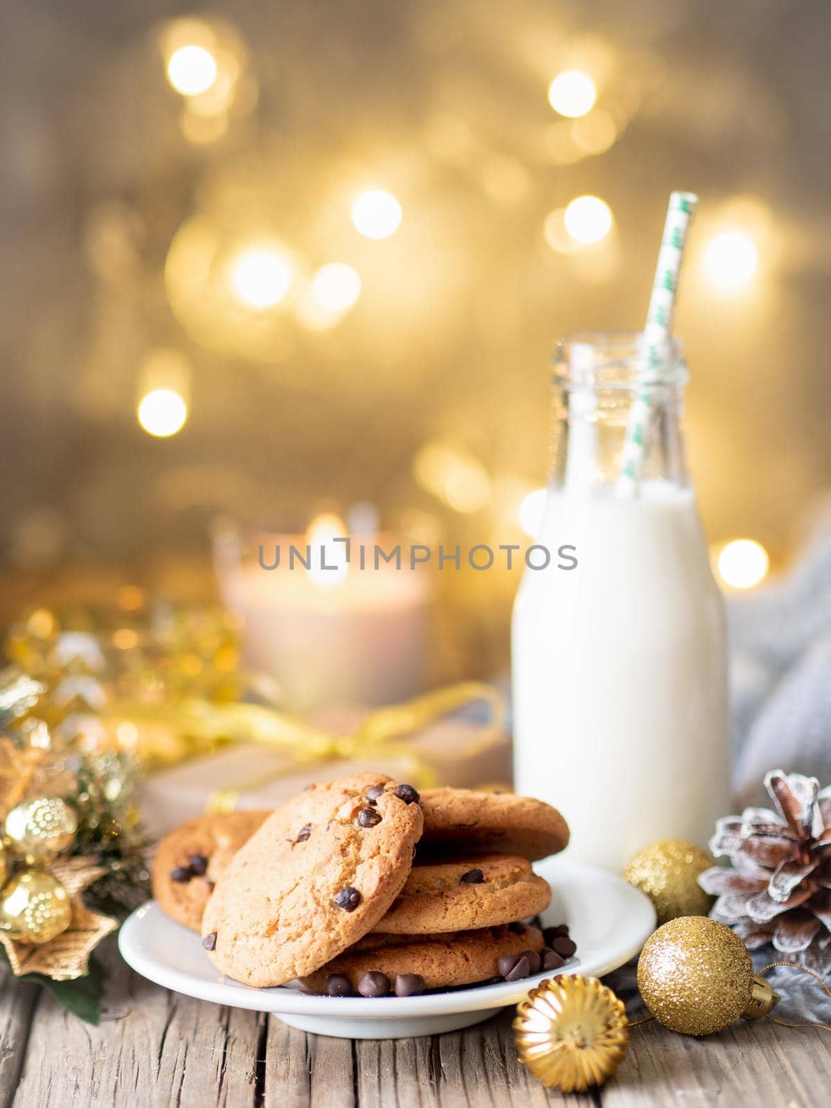 Christmas background with Chocolate chip cookies, bottle with milk. Cozy evening, mug of drink, Christmas decorations, candles and lights garlands.