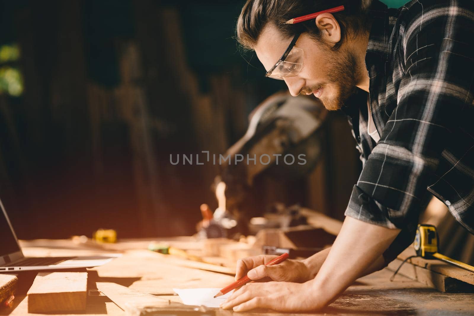 Happy Carpenter smiling to sketch design wooden furniture in wood workshop professional look high skill real authentic handcrafted working people. by qualitystocks