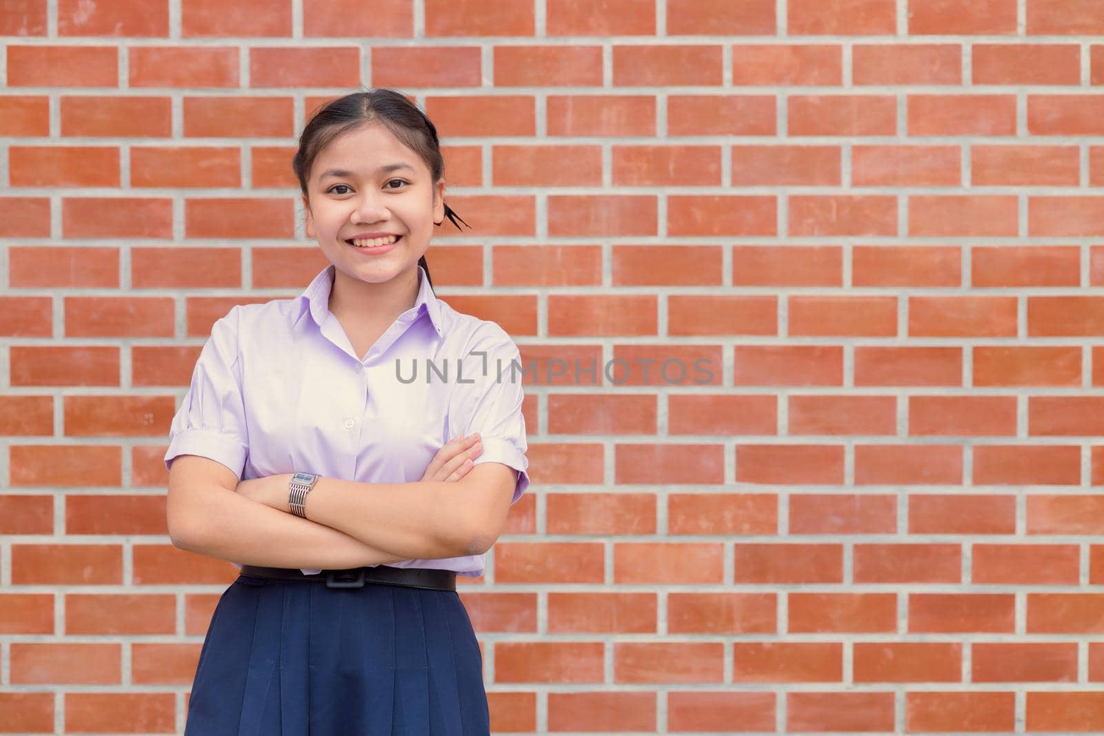 Confident Asian Woman Student  Arm Crossed uniform happy smile with brick wall copy space.