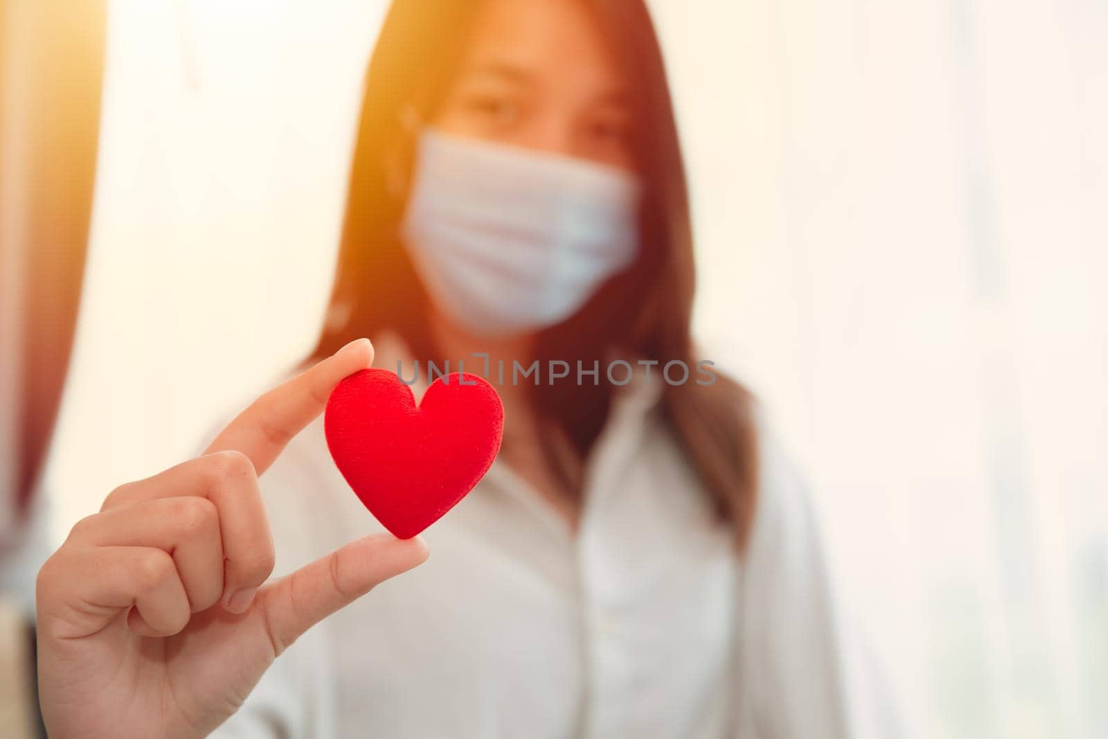 Girl teen wearing face mask hand holding red heart for love care together stay healthy and protect Covid Corona virus spreading concept. by qualitystocks