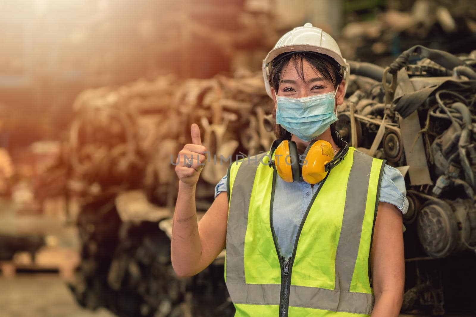Asian women worker thumbs up waring face mask happy working safety work in a heavy industrial factory with engine machine background by qualitystocks