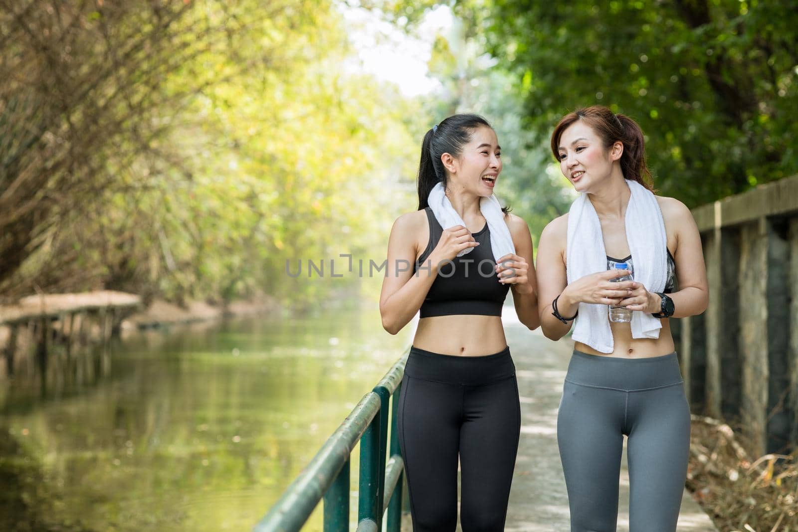 Two Asian adult women outdoors jogging or running in the morning with fresh nature background by qualitystocks