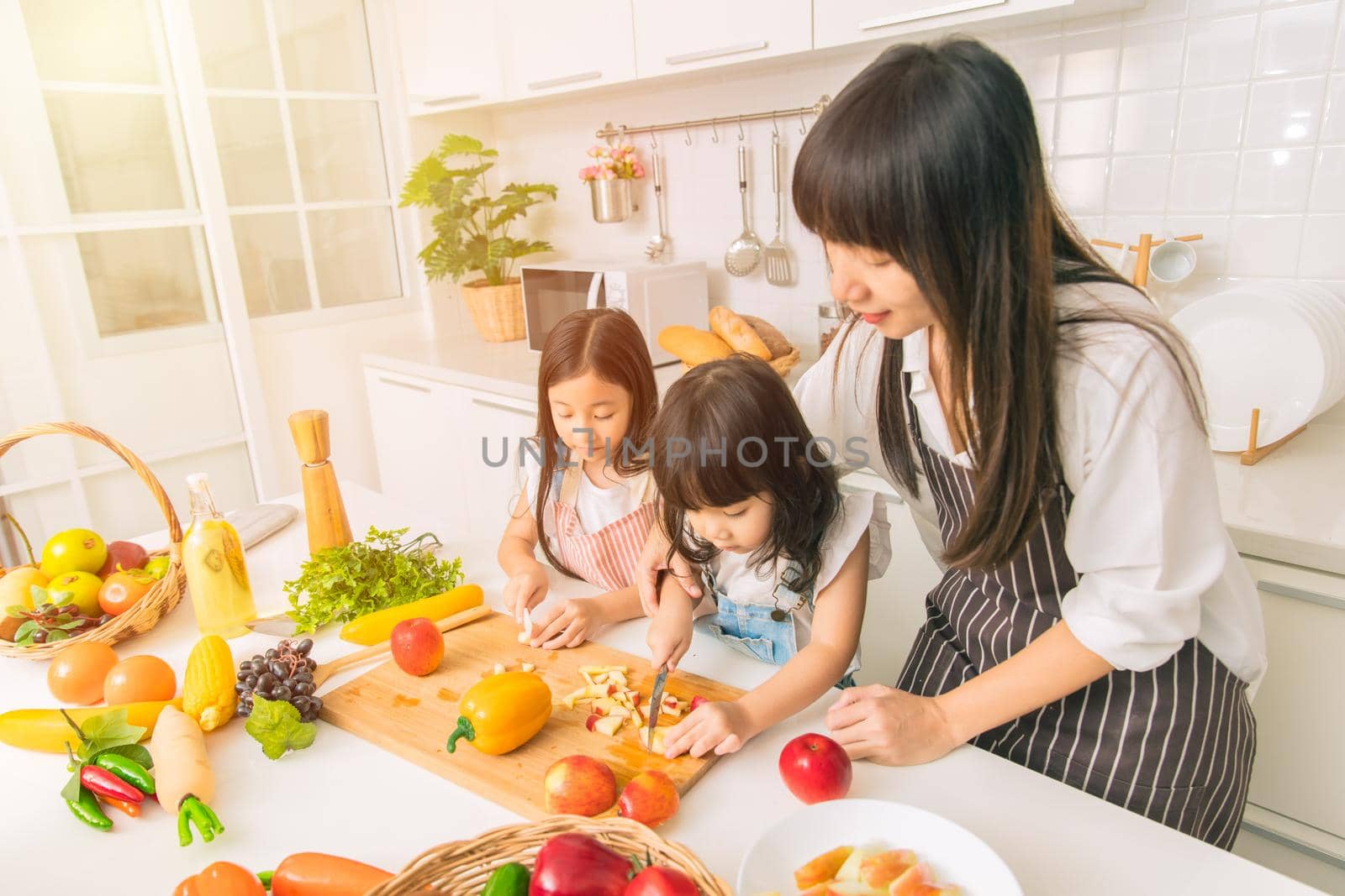 Girl child enjoy playing cut apple together with mother and sister at home kitchen.