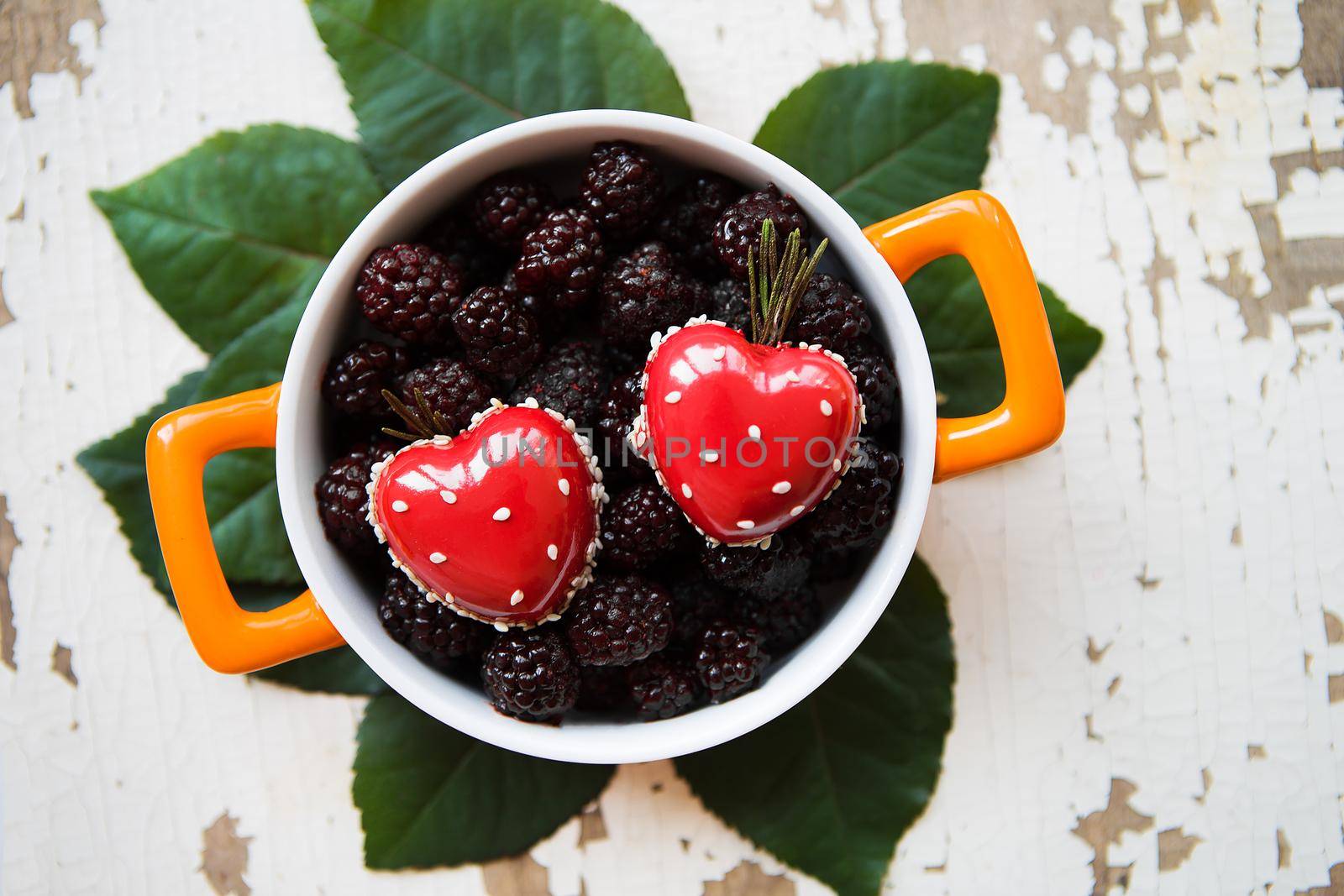 A full blackberry plate with a heart-shaped dessert stands on an old wooden background.