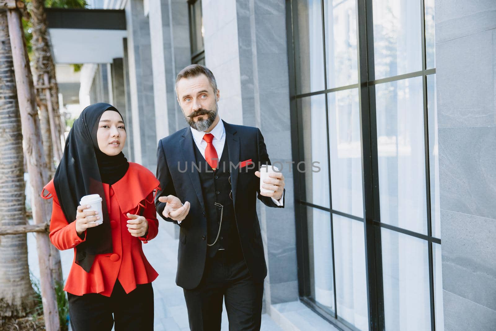 Hispanic Businessman with Asian Arab Muslim business women talking together during coffee break in modern office building.