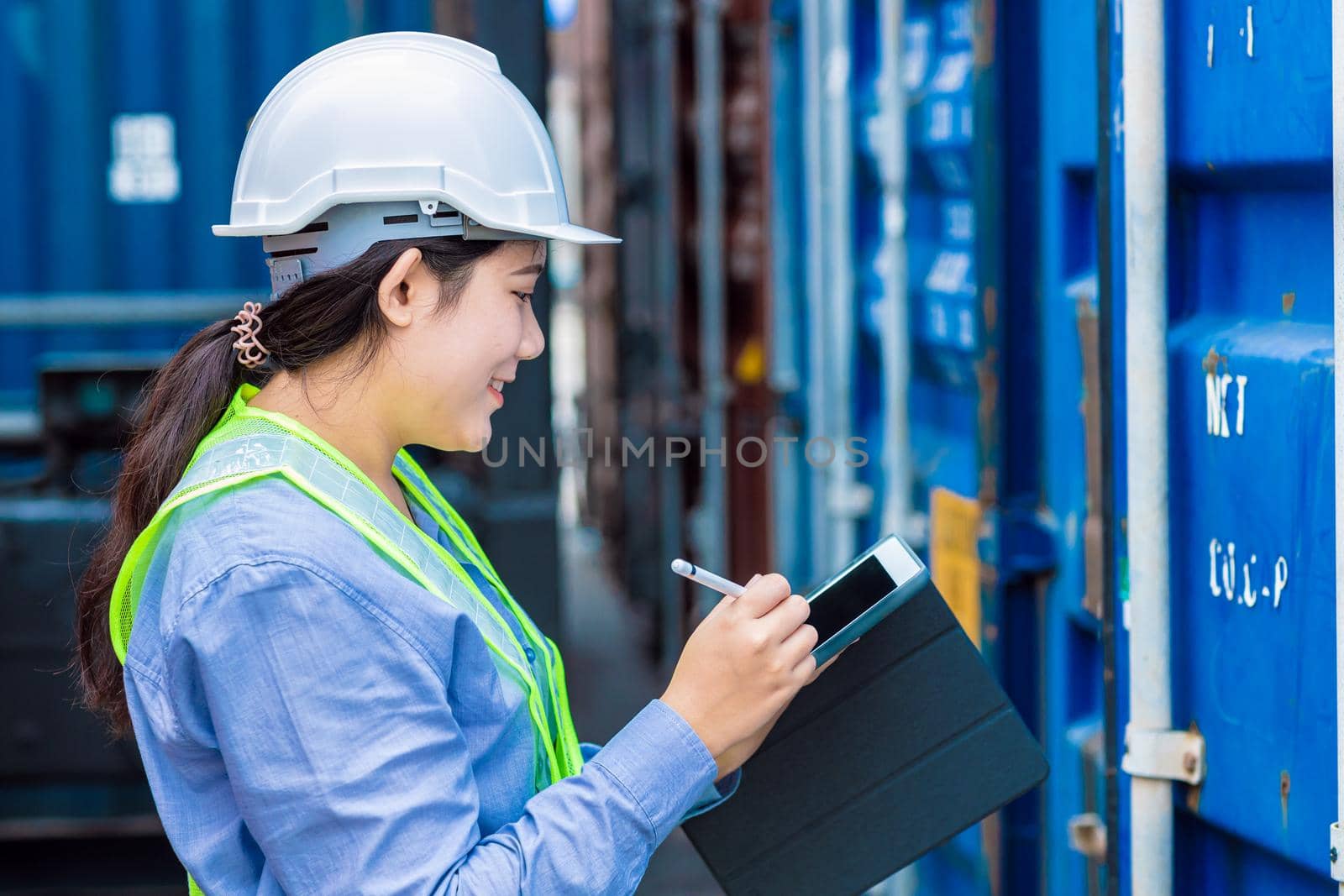Happy woman worker working in port shipping for cargo logistic checking and manage import export goods containers using tablet. by qualitystocks