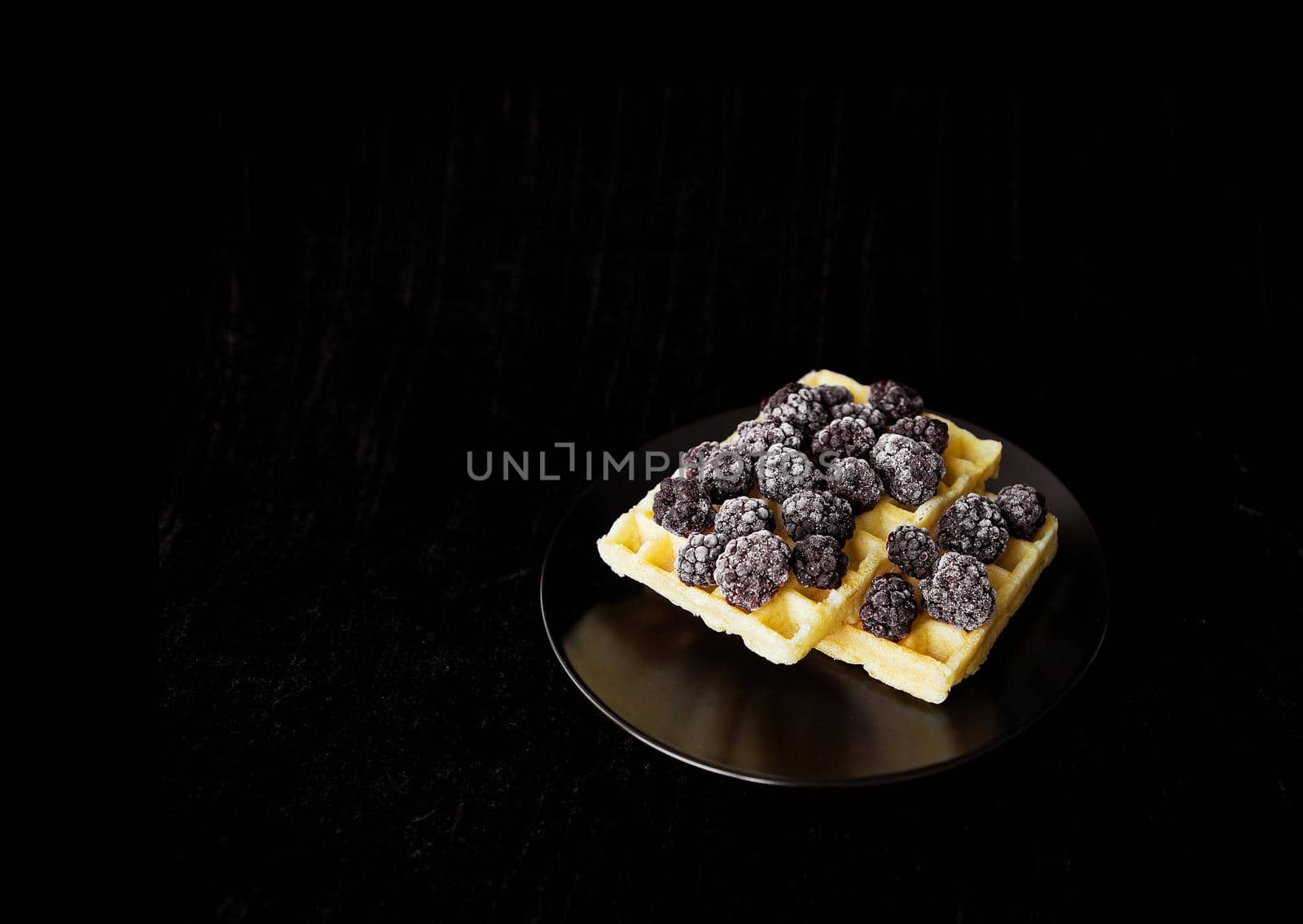 Belgian wafers with frozen blackberries on a black background.