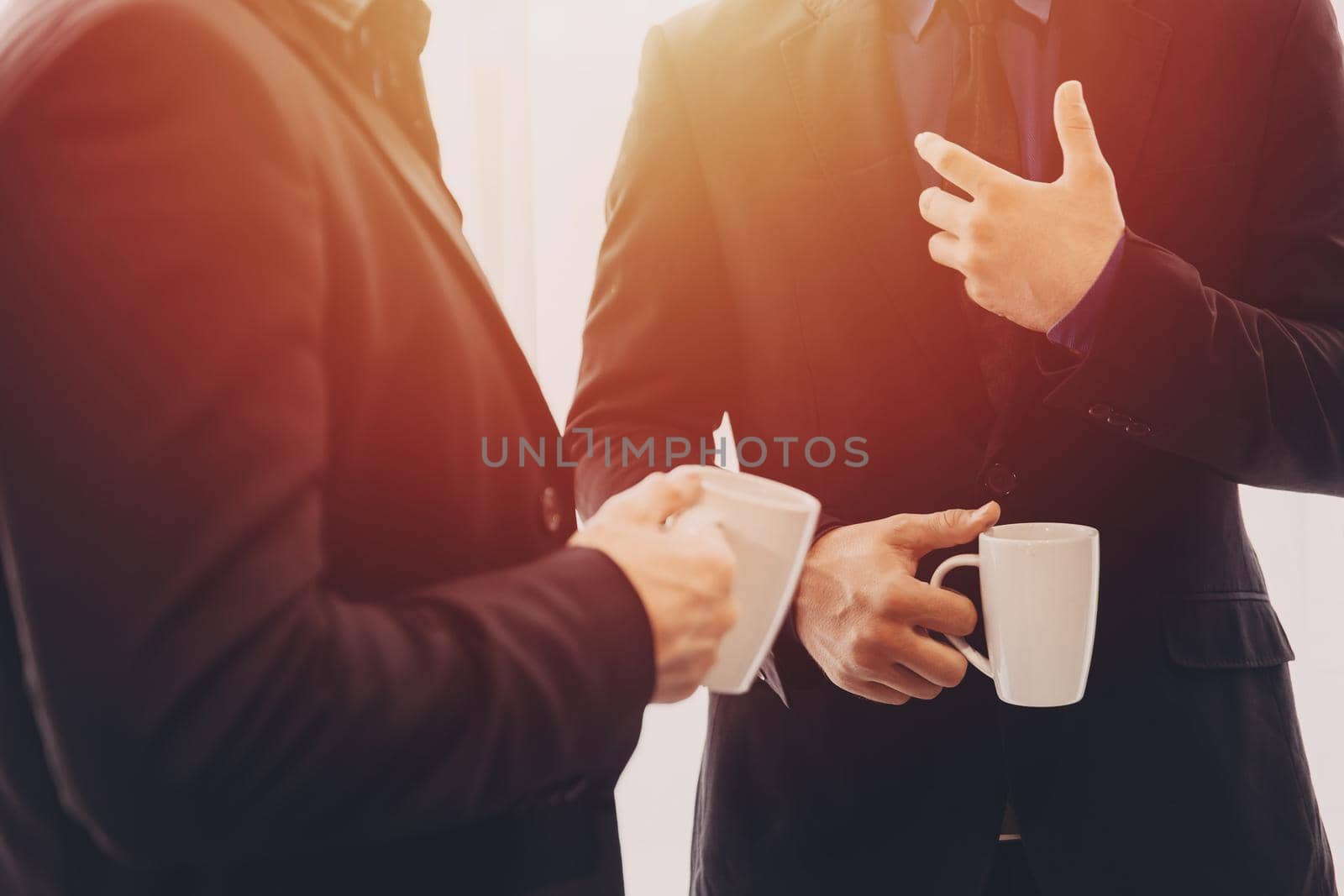 Two Business people standing talking discussion together with morning coffee mug in hand. by qualitystocks