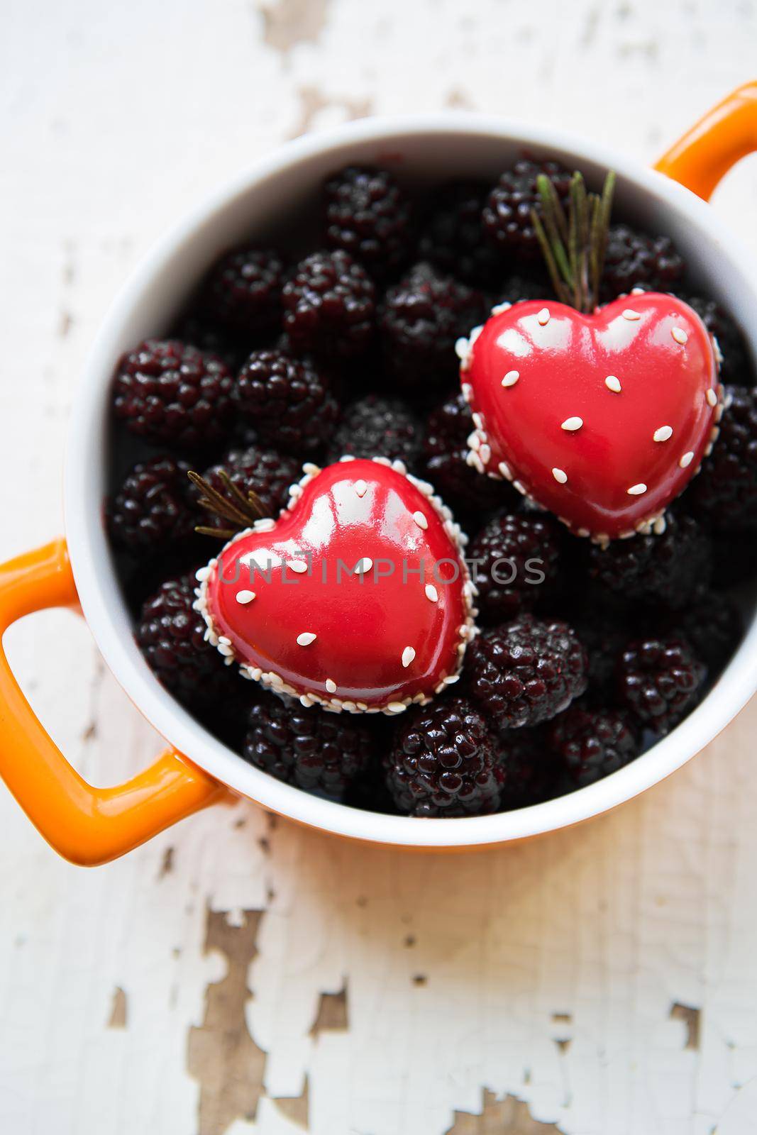 A full blackberry plate with a dessert in the form of a heart stands on a wooden background, close-up.