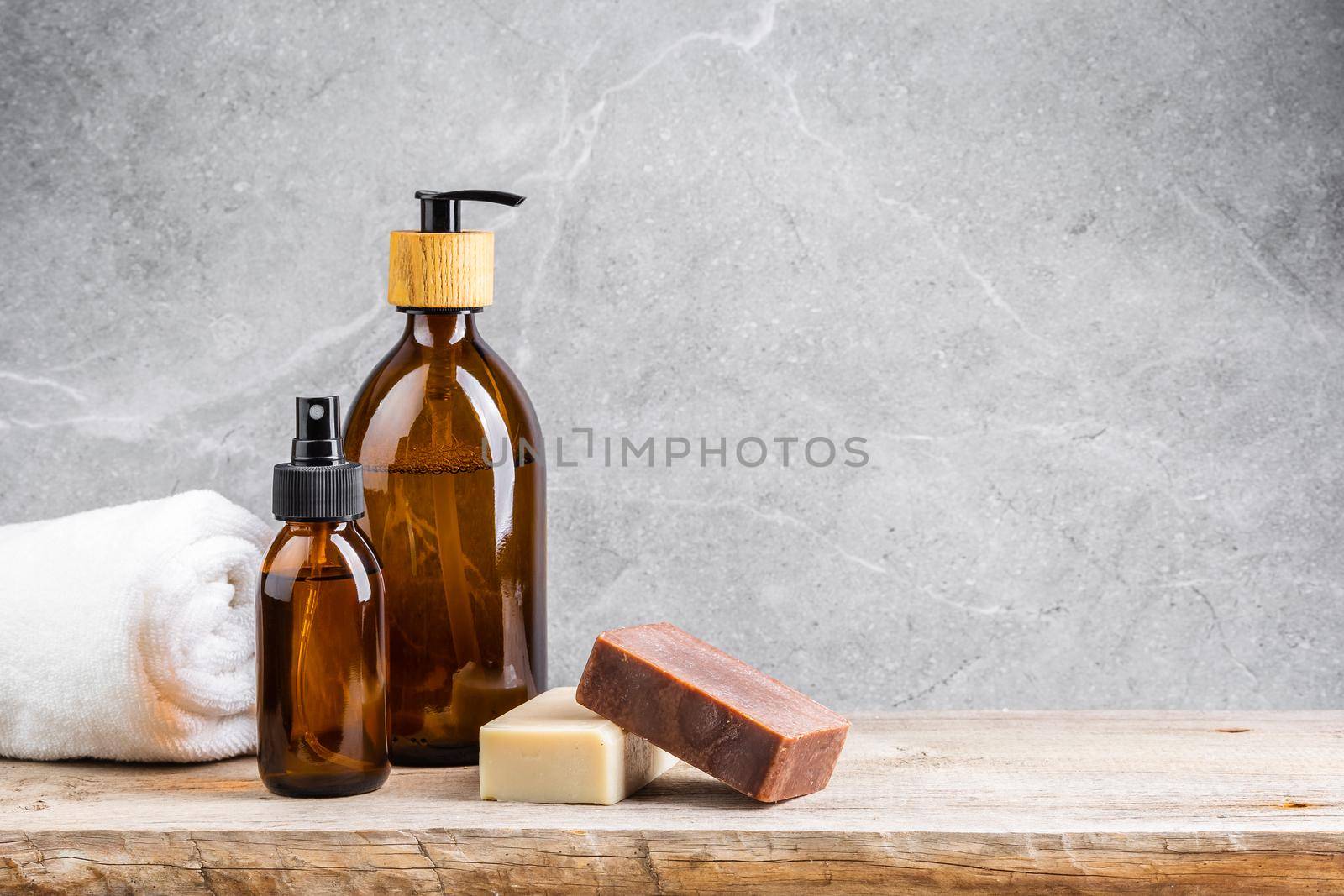 Bathroom table with white towel, dark glass bottles with liquid skin care products and natural handmade solid soap bars over grey marble background
