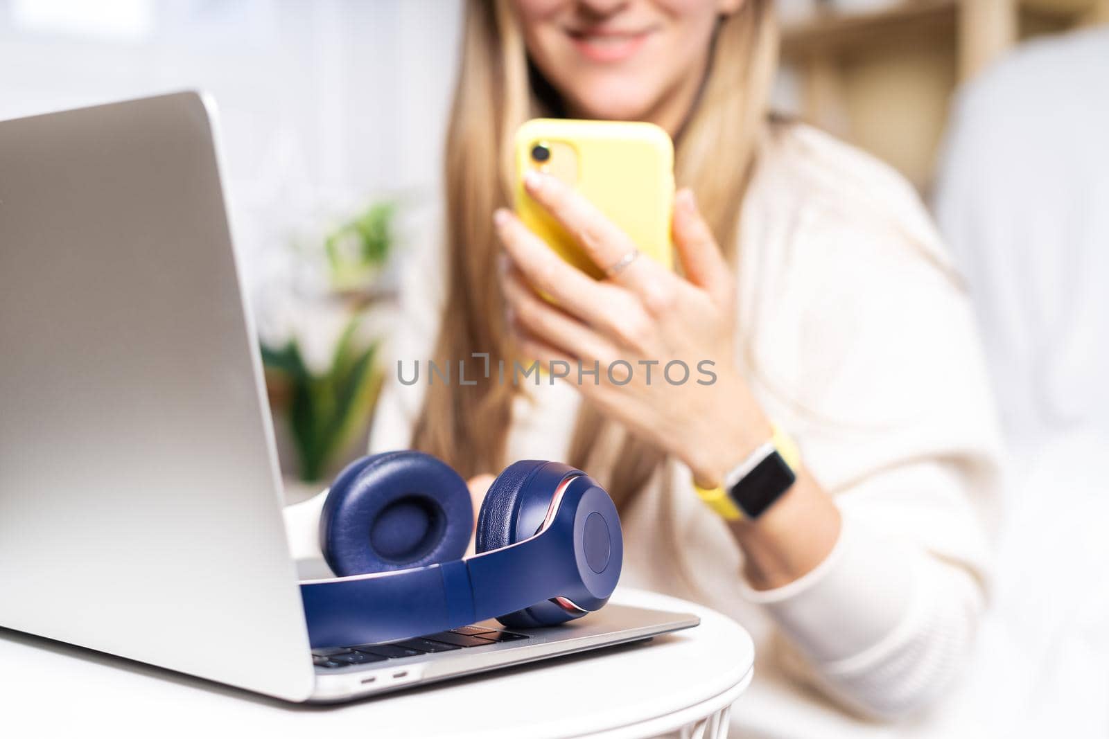 Freelance woman with headphones and laptop, having a video chat at mobile phone. Sitting on the couch, online shopping. Happy girl woking from home office. Distance learning online education and work.