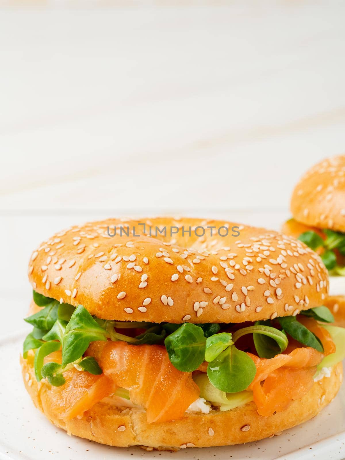 Two sandwiches with salmon, cream cheese, cucumber slices on white marble table, vertical, copy space