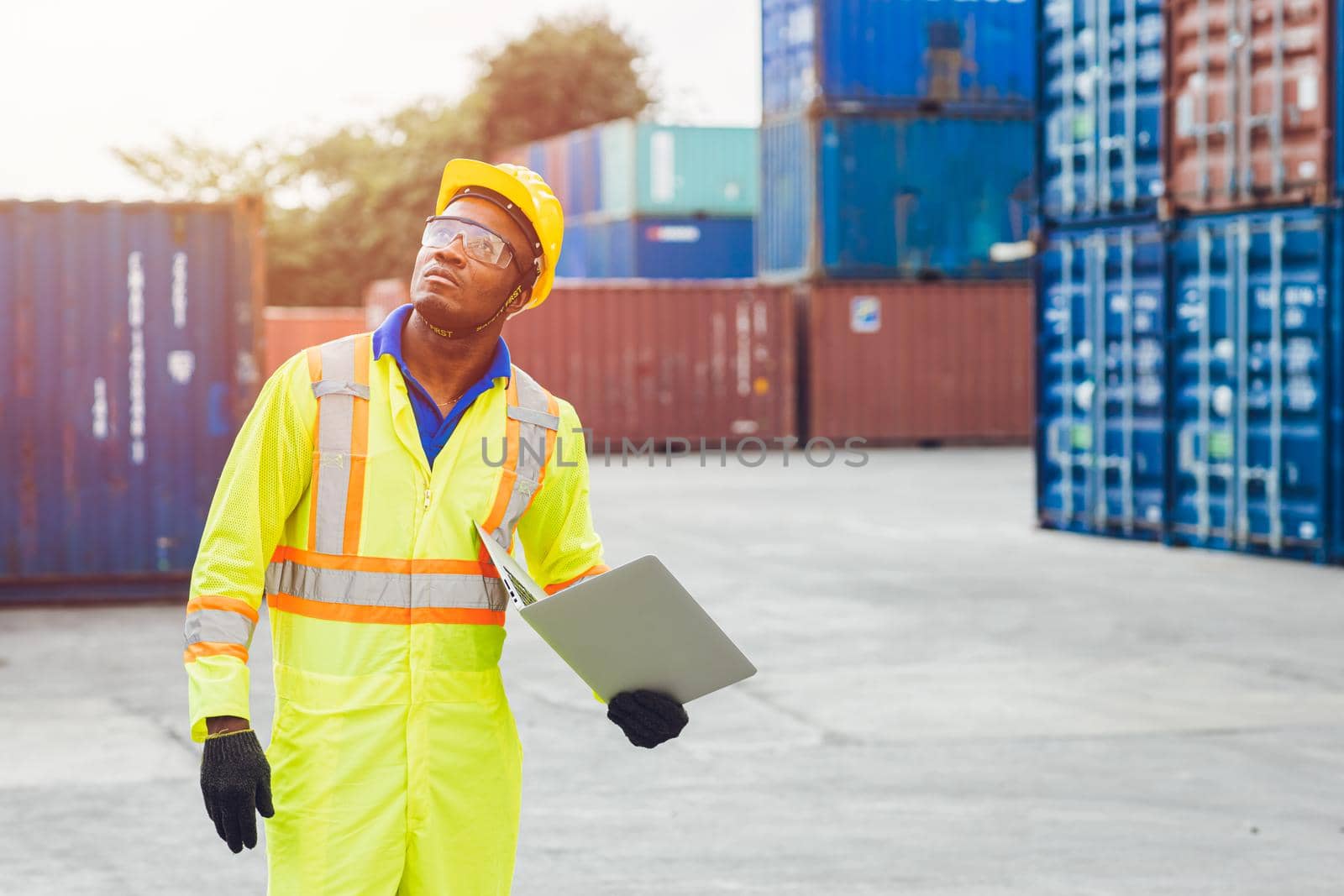 Black African happy worker working in logistic shipping with laptop computer control loading containers at port cargo. Import export shipping industry people.