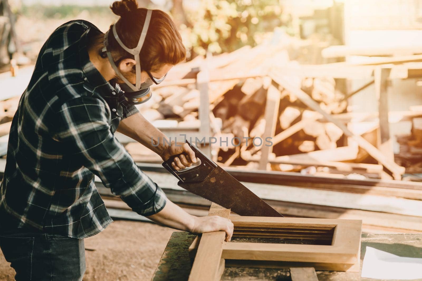 Male worker sawing wood to make furniture in workshop with industry safety air mask.