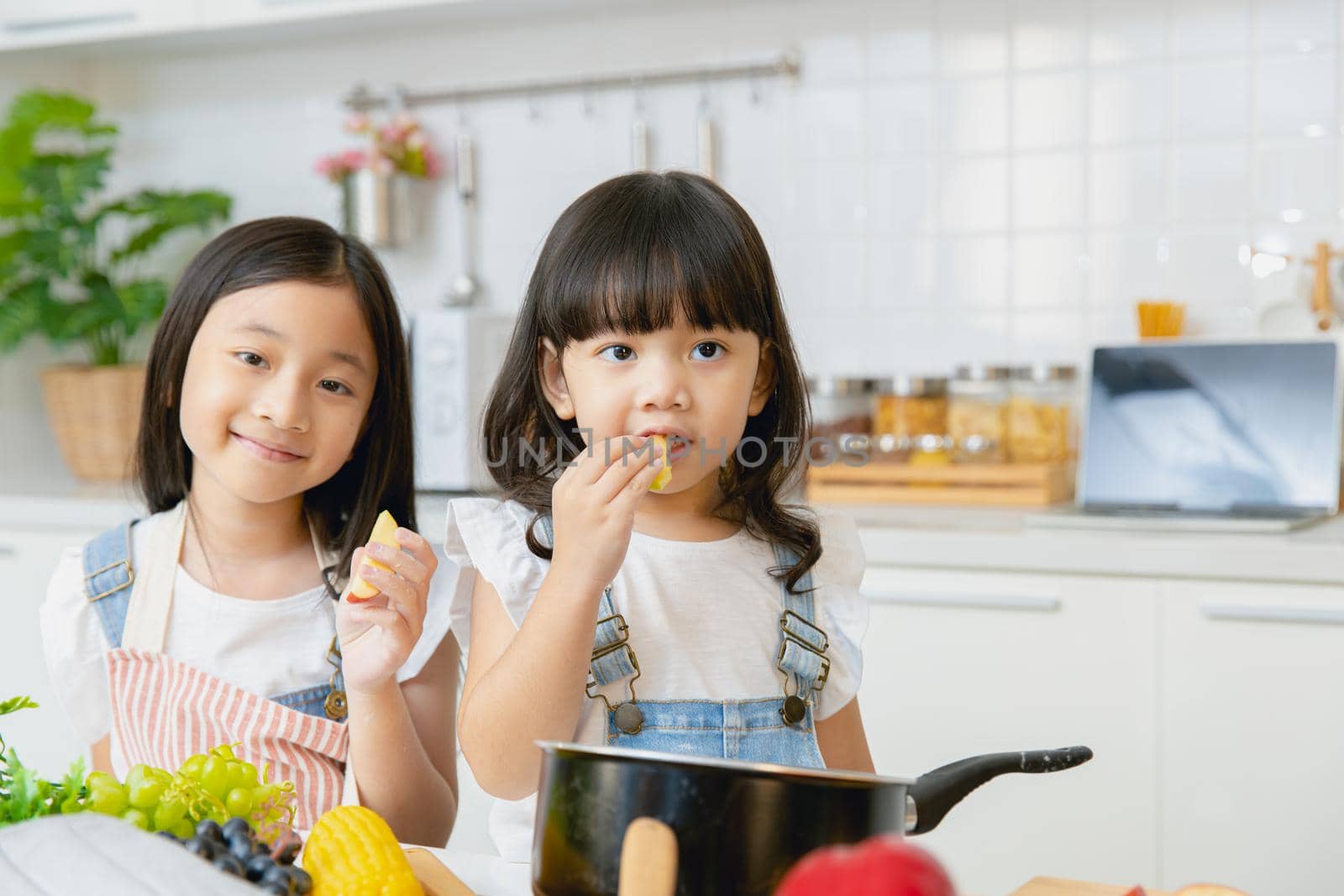Portrait two Asian sister playing and care together eating at home kitchen.