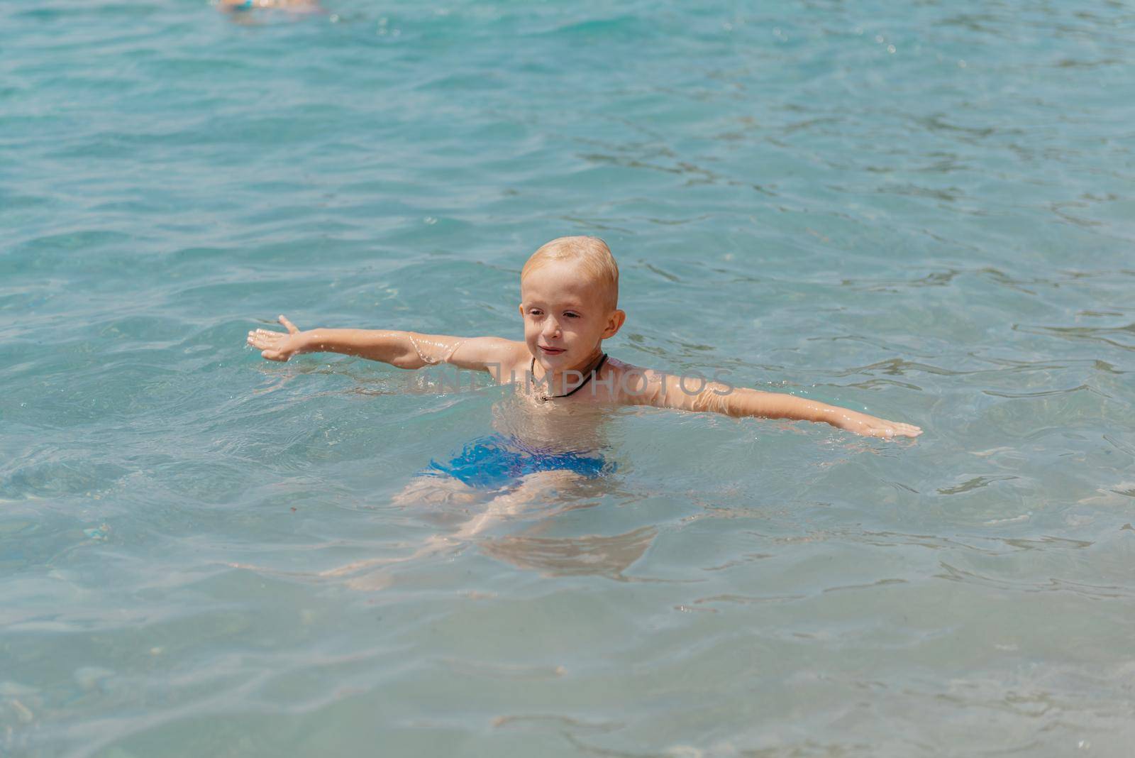 Child learning to swim in the open sea of tropical resort. Kids learn swimming. Exercise and training for young children. Little boy with colorful float board in sport club. Swimming baby or toddler. Happy child boy swims in sea in swimming circle with splash. Blue sky and water. Swimming training. Fun joy activities on vacation in the beach. Childhood moments lifestyle. Freedom careless. boy swim in the sea by Andrii_Ko