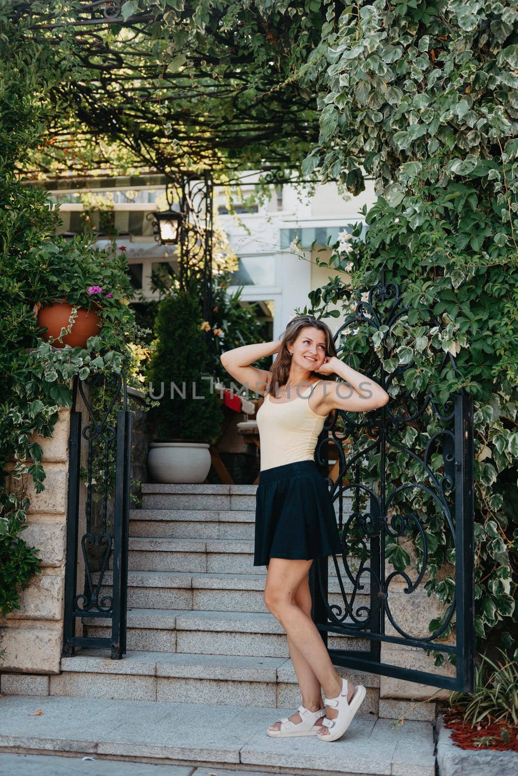 Girl tourist walking through ancient narrow street on a beautiful summer day in MEDITERRANEAN MEDIEVAL CITY , OLD TOWN bUDVA, MONTENEGRO. Young beautiful cheerful woman walking on old street at tropical town. Pretty girl looking at you and smiling