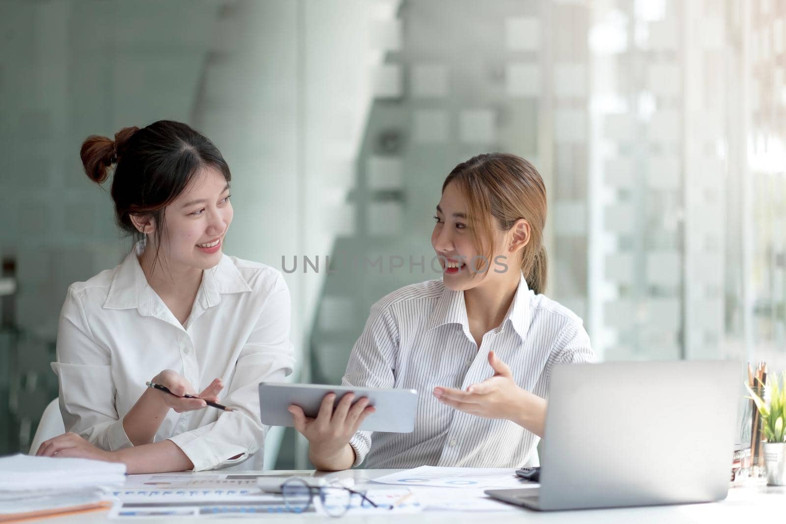 Two asian business woman work together to get the job done at the office. by wichayada