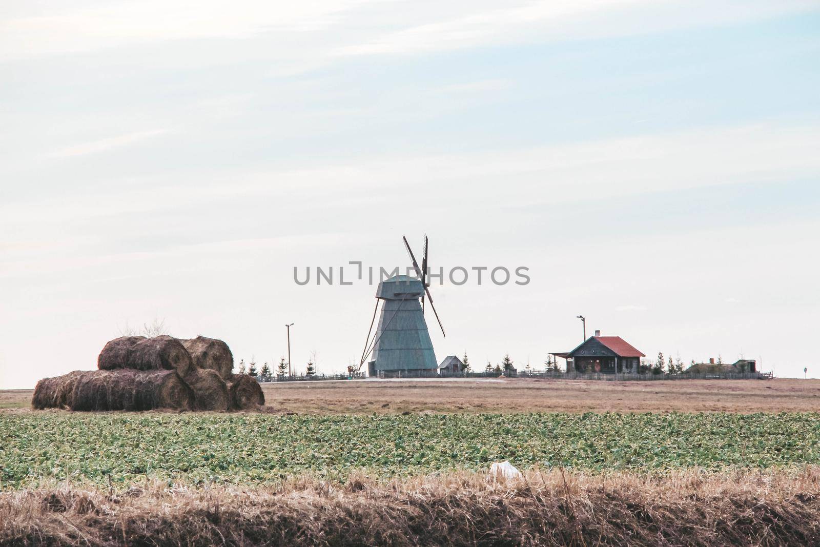 Vintage windmill in a field with hay bales and modern building . High quality photo