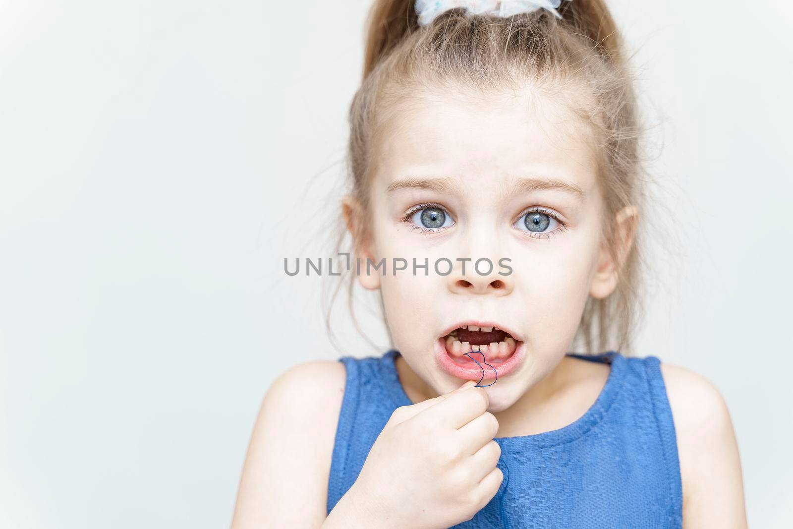 Cute scared girl pulling her loose tooth using a string by Lena_Ogurtsova