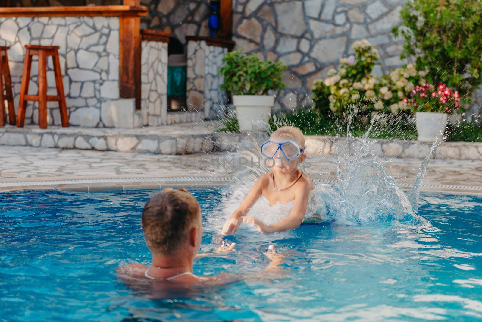 Excited boy in googles jumping in water from shoulders of his father standing in swimming pool