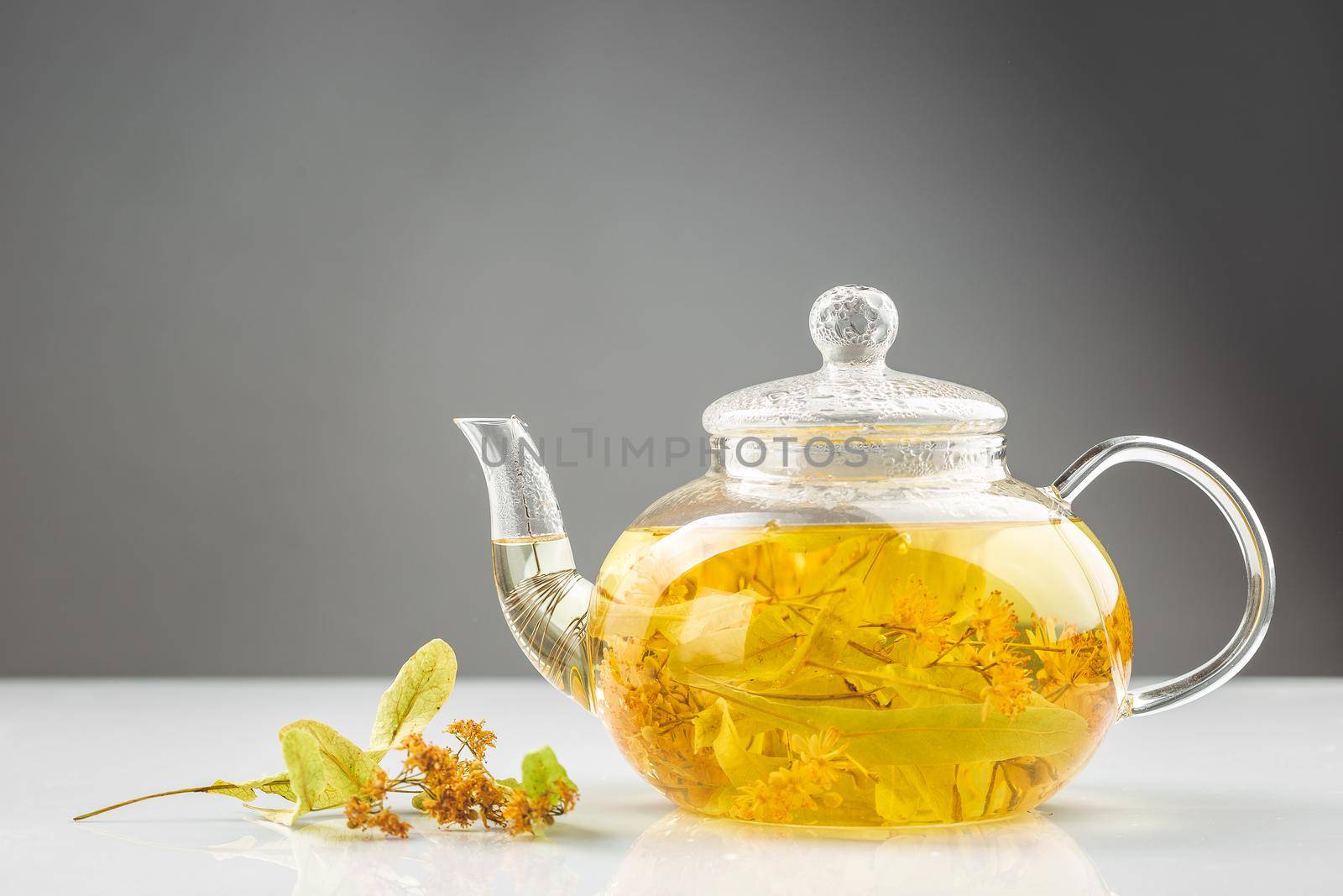 Transparent teapot with linden or tilia tea flowers brewed with hot water 