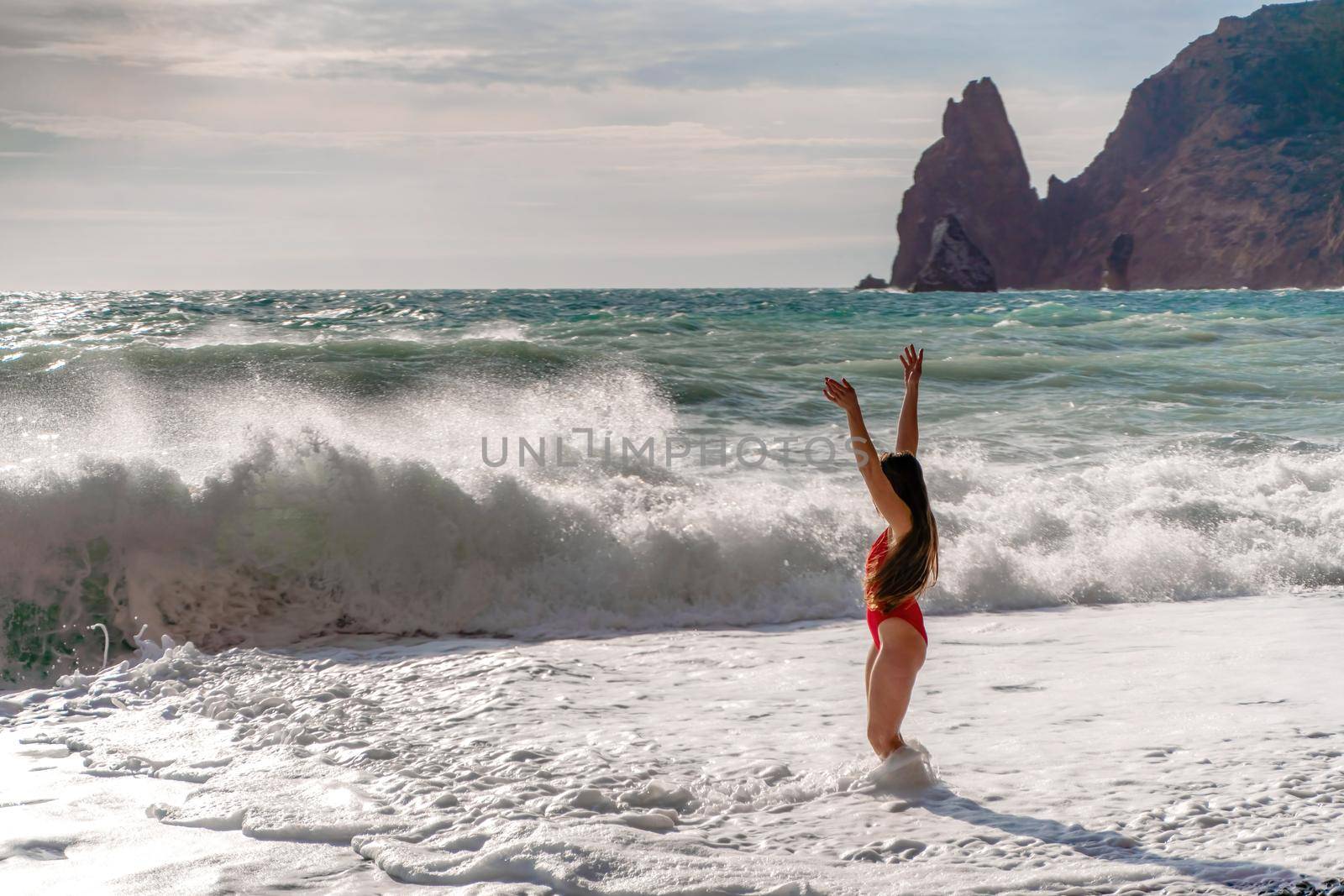 A beautiful and sexy brunette in a red swimsuit on a pebble beach, Running along the shore in the foam of the waves.