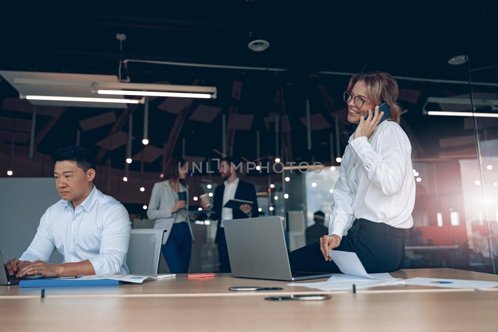 Business woman talking on phone after meeting in modern office with colleagues in the background