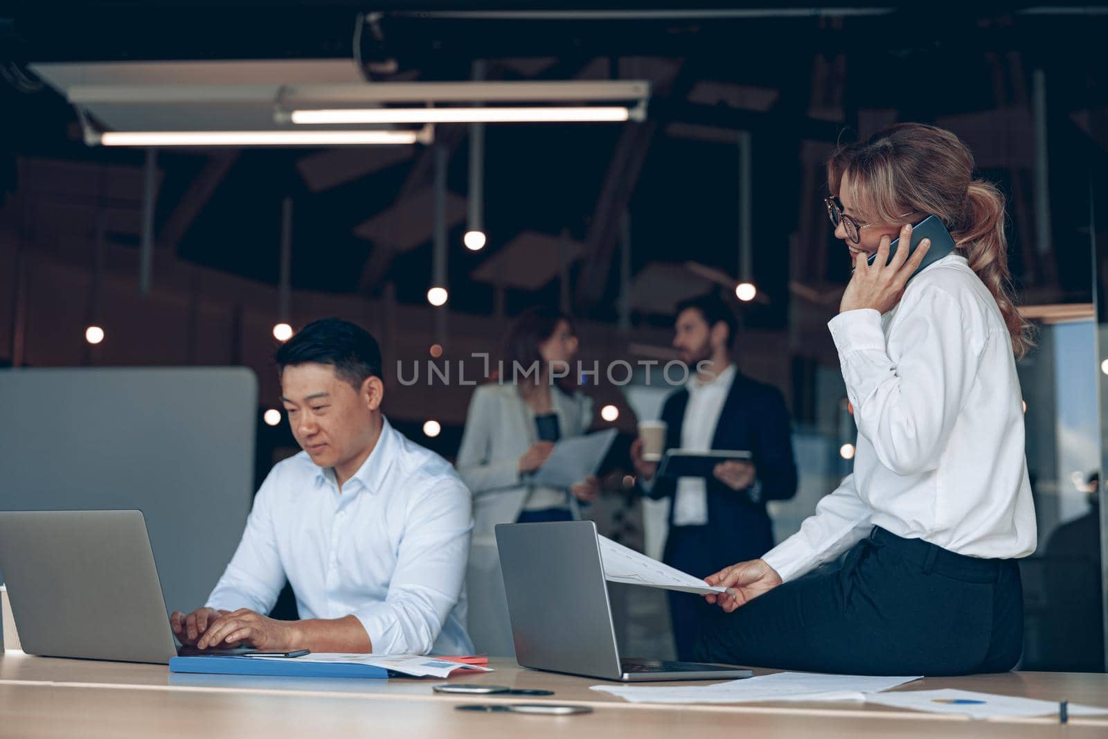 business woman sitting on table and talking phone to solve problem with colleagues in the background
