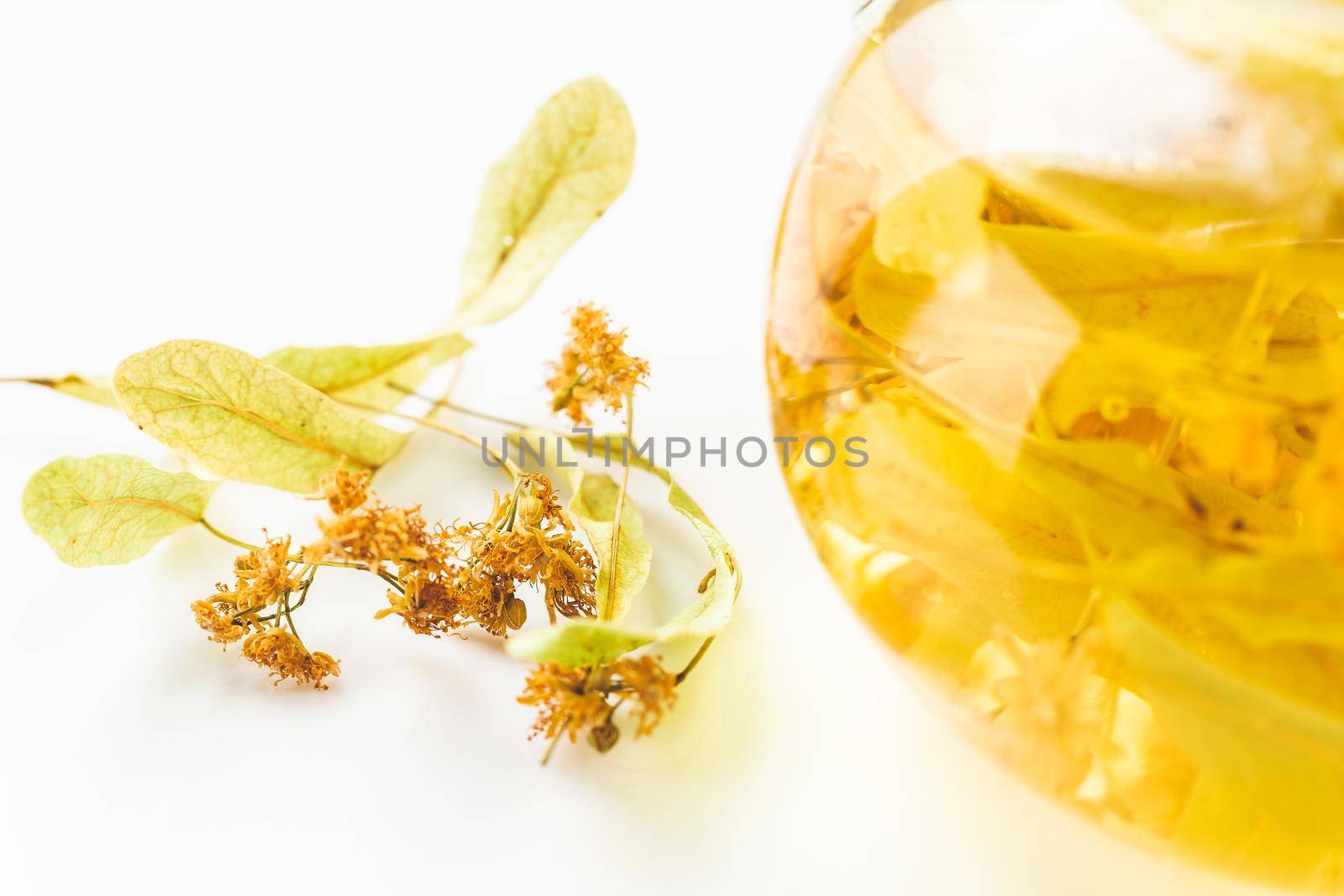 Transparent teapot with linden or tilia tea flowers brewed with hot water 