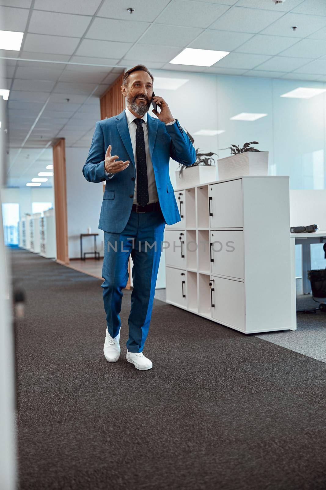 Happy businessman wearing suit walking in the office and talking on smartphone