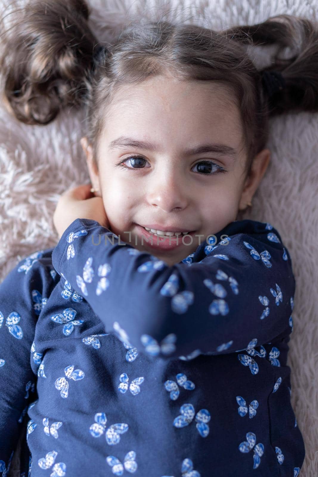 Middle Eastern young cute girl lies on a light bed in the light of sunlight. Persian swarthy girl on the bed. Middle Eastern kids on the bed
