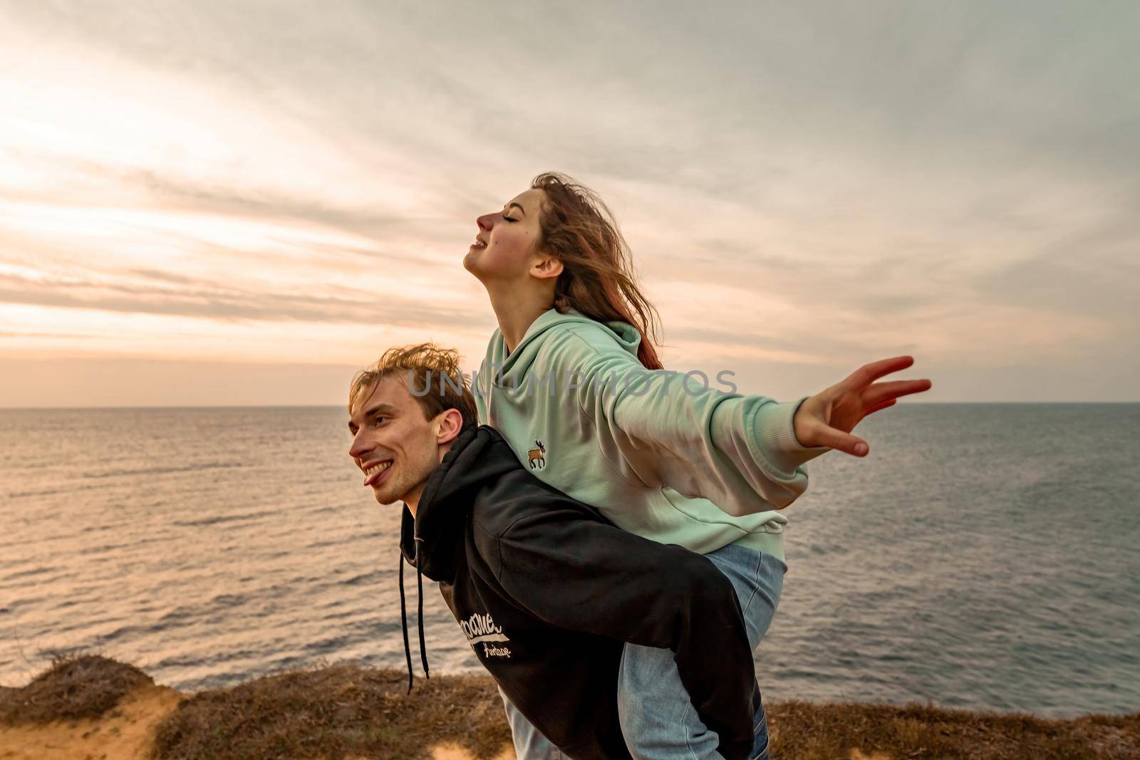 Portraits of lovers, romantic couple of lovers hugging, kissing, touching, eye contact at sunset, sunrise against the background of the sea, sun, clouds in fiery red, orange colors.