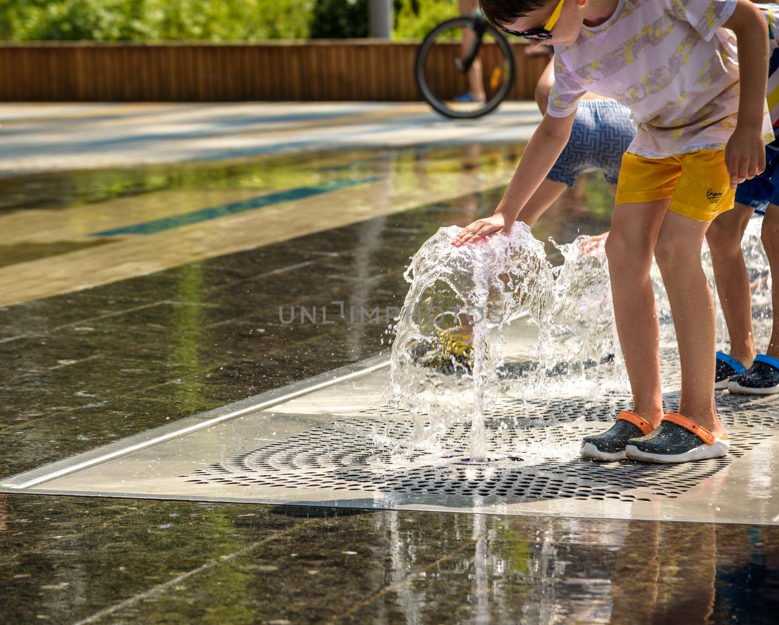 Kyiv, Ukraine - August 01, 2021: Boys jumping in water fountains. Children playing with a city fountain on hot summer day. Happy friends having fun in fountain. Summer weather. Friendship, lifestyle and vacation.