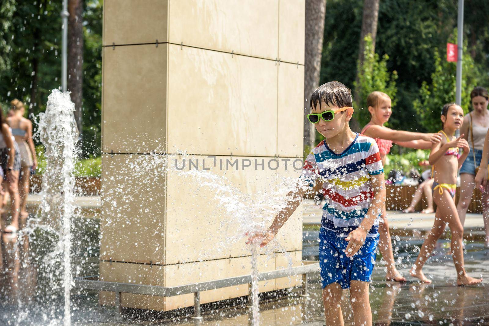 Kyiv, Ukraine - August 01, 2021: Boys jumping in water fountains. Children playing with a city fountain on hot summer day. Happy friends having fun in fountain. Summer weather. Friendship, lifestyle and vacation.