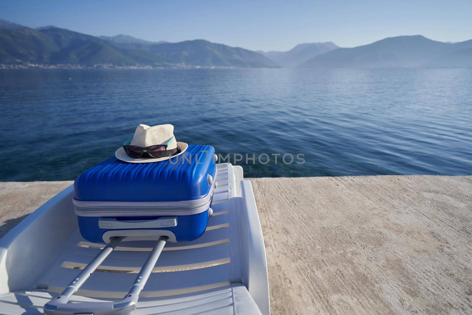 Blue suitcase on a sun lounger on the shore of the adriatic sea in Montenegro, travel concept.