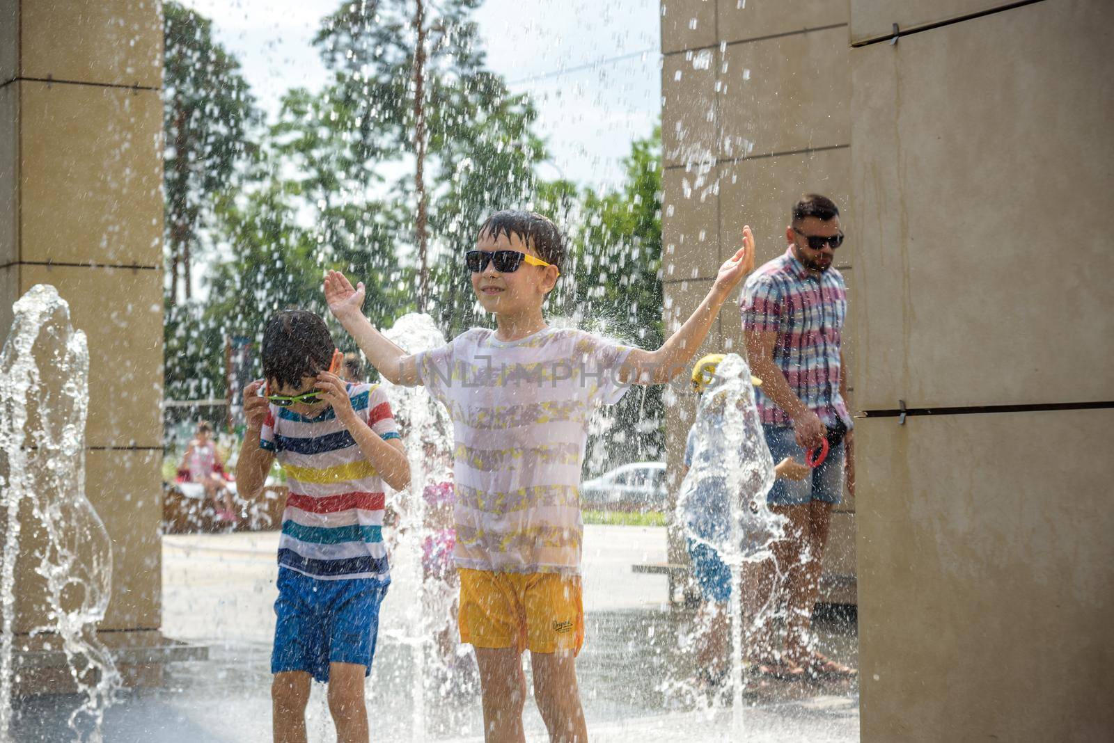 Kyiv, Ukraine - August 01, 2021: Boys jumping in water fountains. Children playing with a city fountain on hot summer day. Happy friends having fun in fountain. Summer weather. Friendship, lifestyle and vacation.