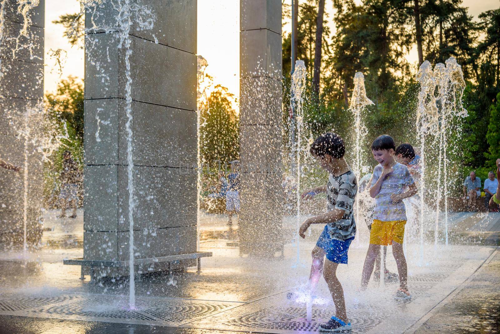 Kyiv, Ukraine - August 01, 2021: Boys jumping in water fountains. Children playing with a city fountain on hot summer day. Happy friends having fun in fountain. Summer weather. Friendship, lifestyle and vacation.