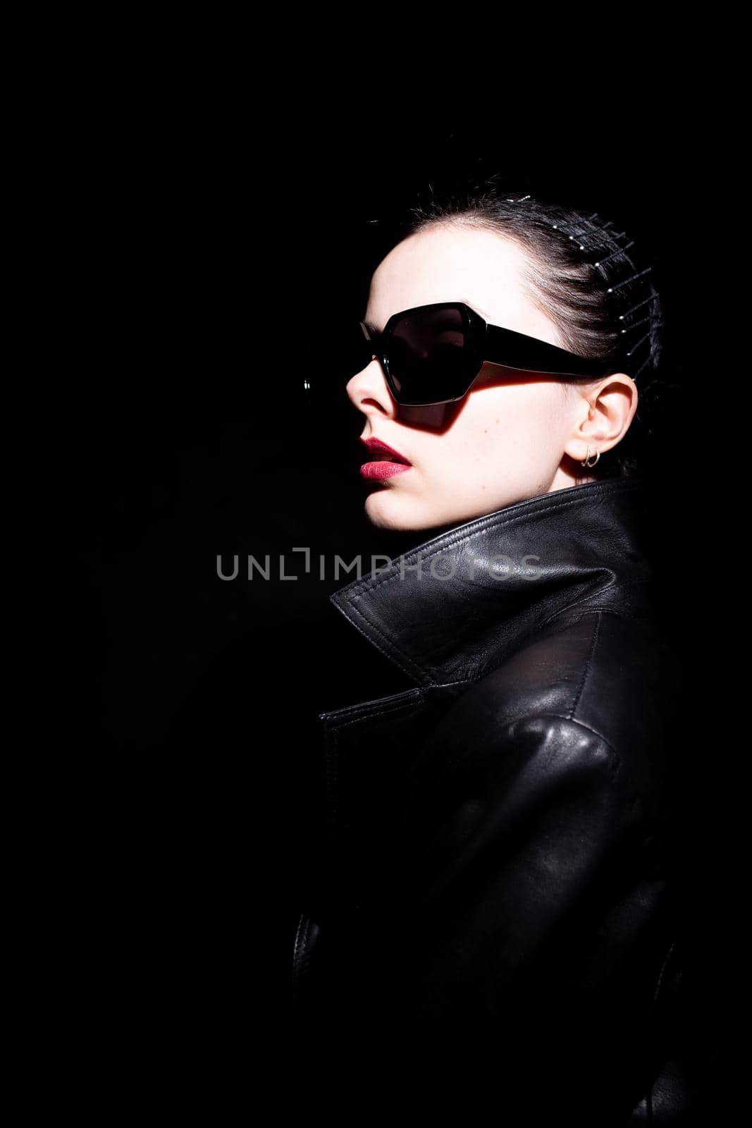woman in leather coat and black sunglasses, black background. High quality photo