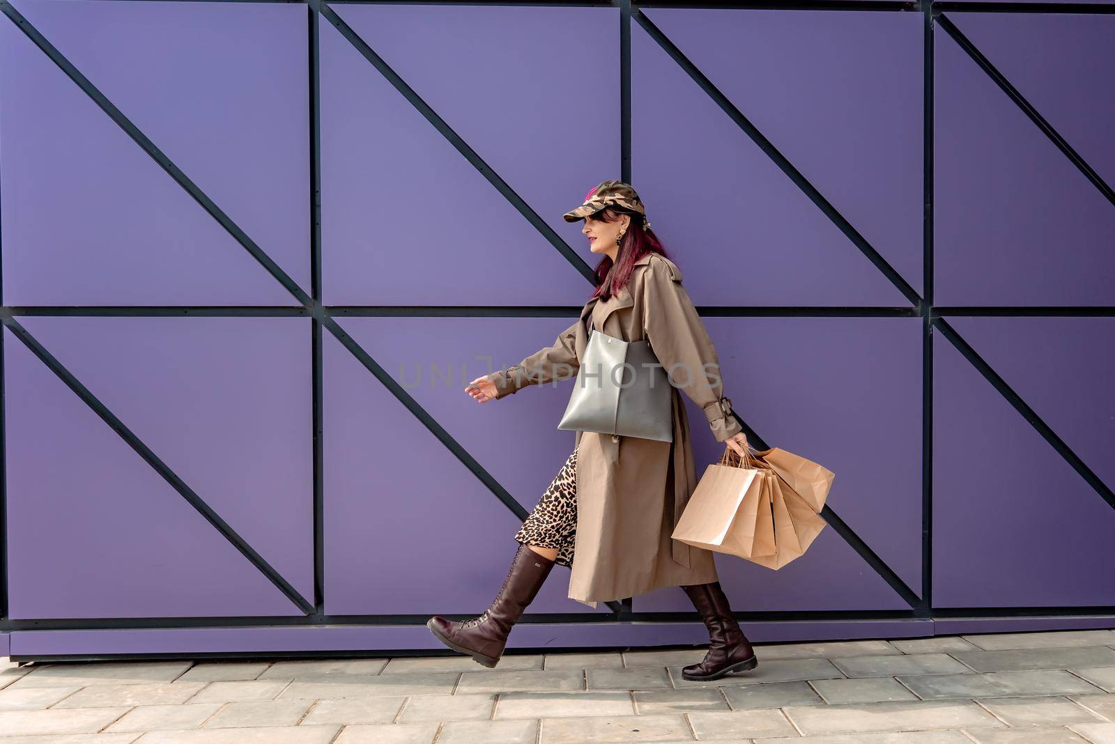 A happy shopaholic girl keeps her bags near the shopping center. A woman near the store is happy with her purchases, holding bags. Dressed in a leopard print dress. Consumer concept