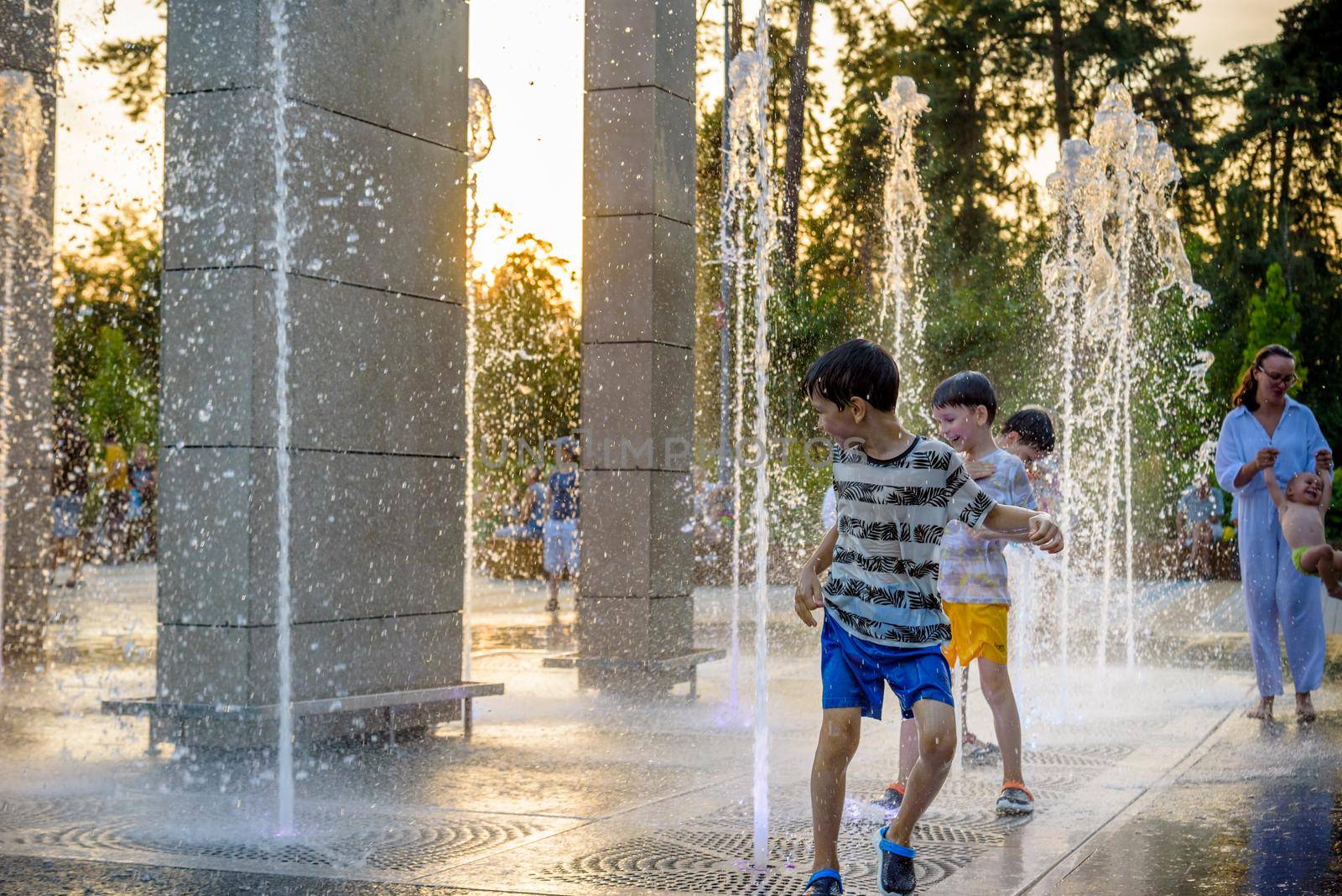 Kyiv, Ukraine - August 01, 2021: Boys jumping in water fountains. Children playing with a city fountain on hot summer day. Happy friends having fun in fountain. Summer weather. Friendship, lifestyle and vacation.