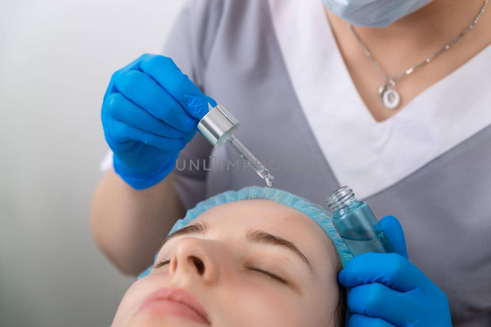 Hands of cosmetologist dripping nourishing oil facial skin of young woman in spa salon. Facial treatment and skincare concept.