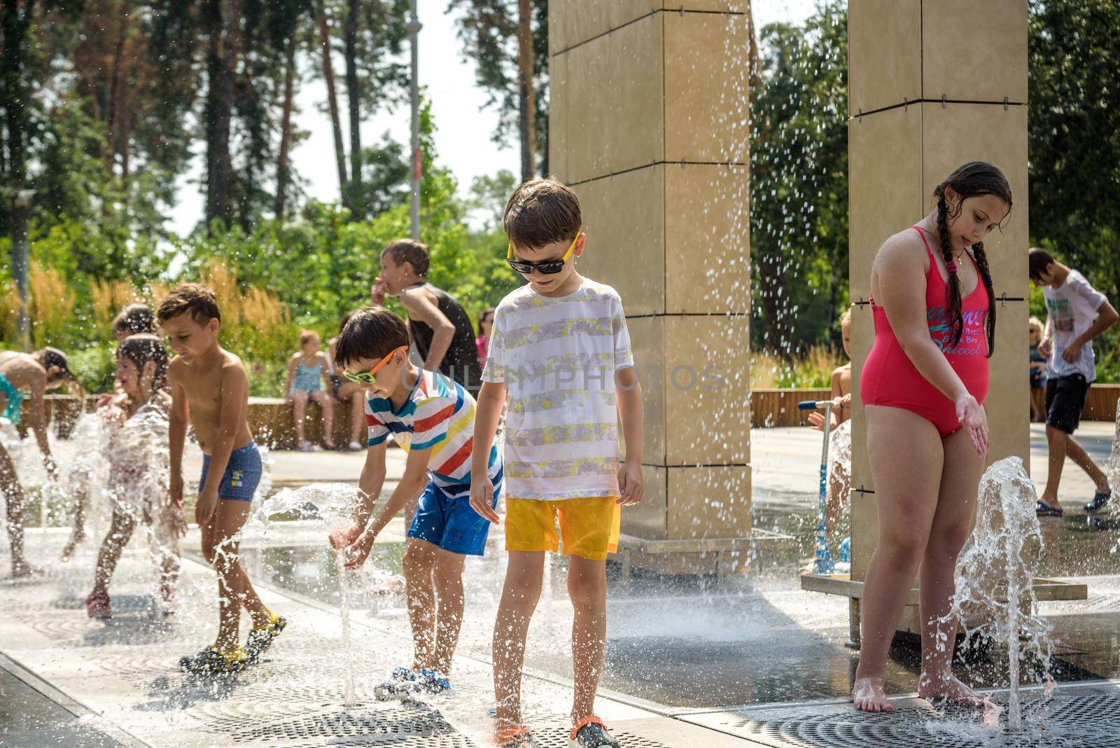 Kyiv, Ukraine - August 01, 2021: Boys jumping in water fountains. Children playing with a city fountain on hot summer day. Happy friends having fun in fountain. Summer weather. Friendship, lifestyle and vacation.