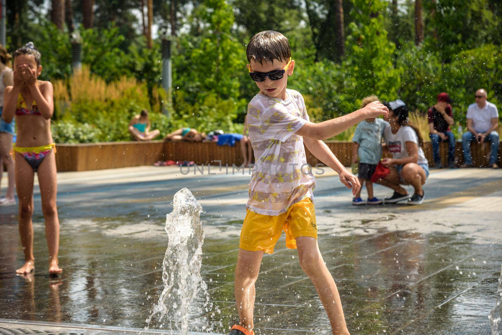 Kyiv, Ukraine - August 01, 2021: Boys jumping in water fountains. Children playing with a city fountain on hot summer day. Happy friends having fun in fountain. Summer weather. Friendship, lifestyle and vacation.