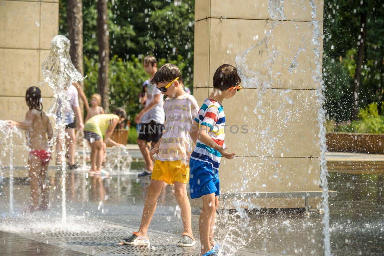 Kyiv, Ukraine - August 01, 2021: Boys jumping in water fountains. Children playing with a city fountain on hot summer day. Happy friends having fun in fountain. Summer weather. Friendship, lifestyle and vacation.