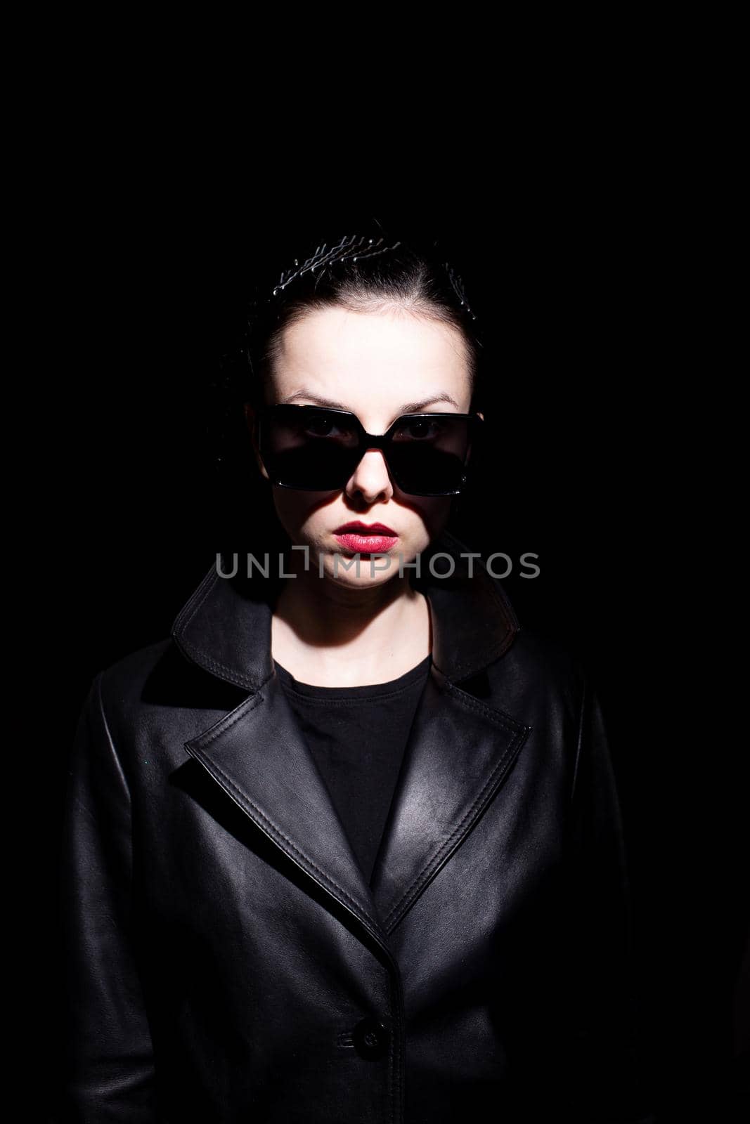 woman in leather coat and black sunglasses, black background. High quality photo