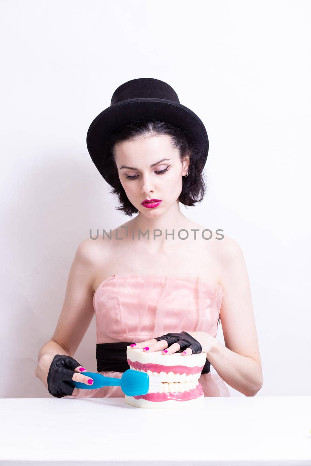 A woman in a dress and hat sits at a table and holds a mock-up of her teeth. High quality photo