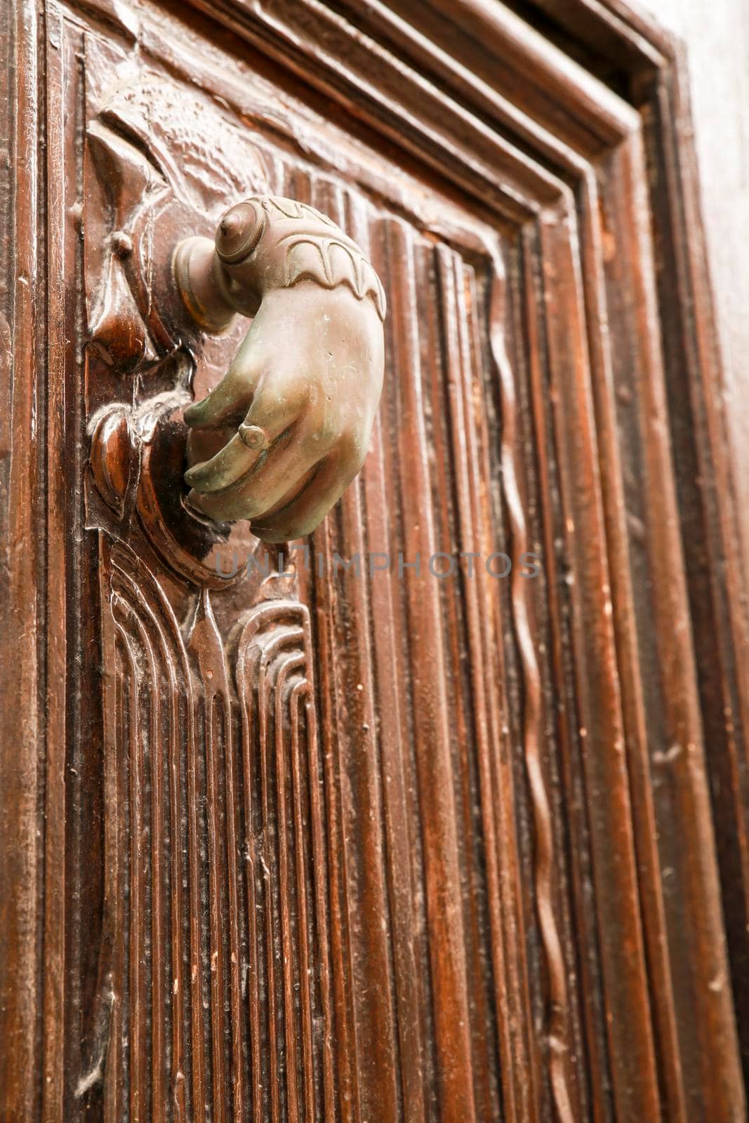 Golden doorknocker with hand shape on old wooden door by soniabonet